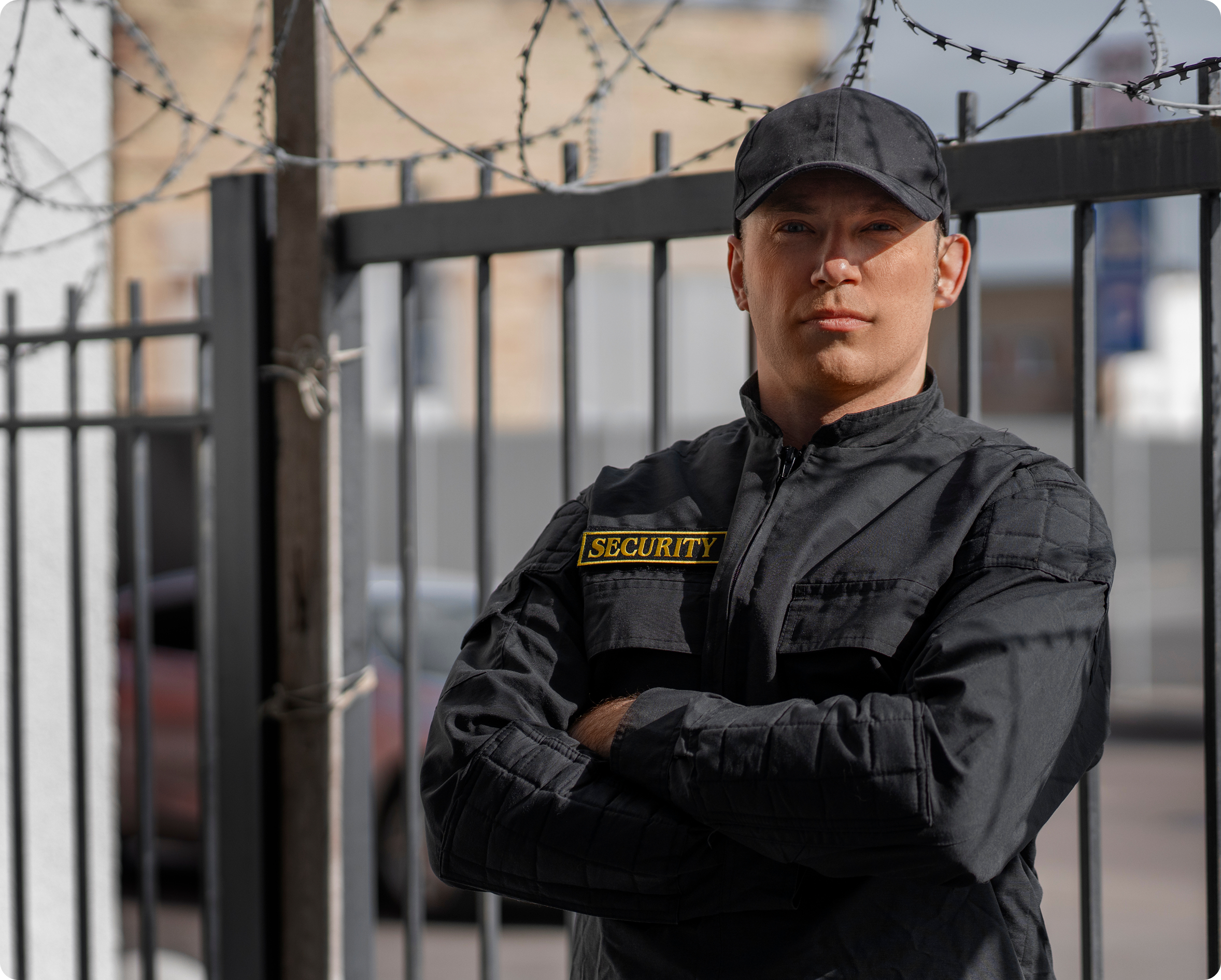 Armed security officer in uniform standing with arms crossed near a secured perimeter